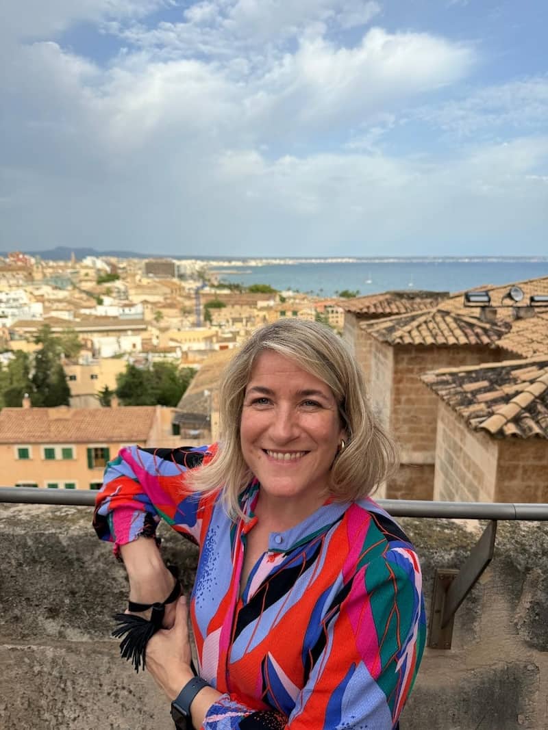 Woman in a colorful shirt standing on a rooftop with a scenic view of a city and sea.