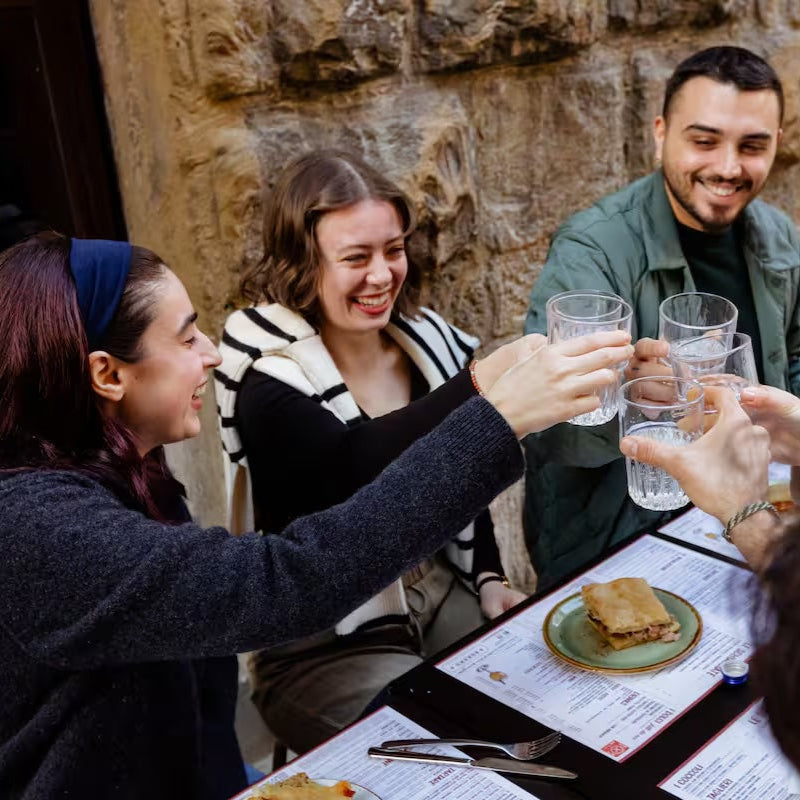 Group of people toasting with drinks at an outdoor restaurant table.