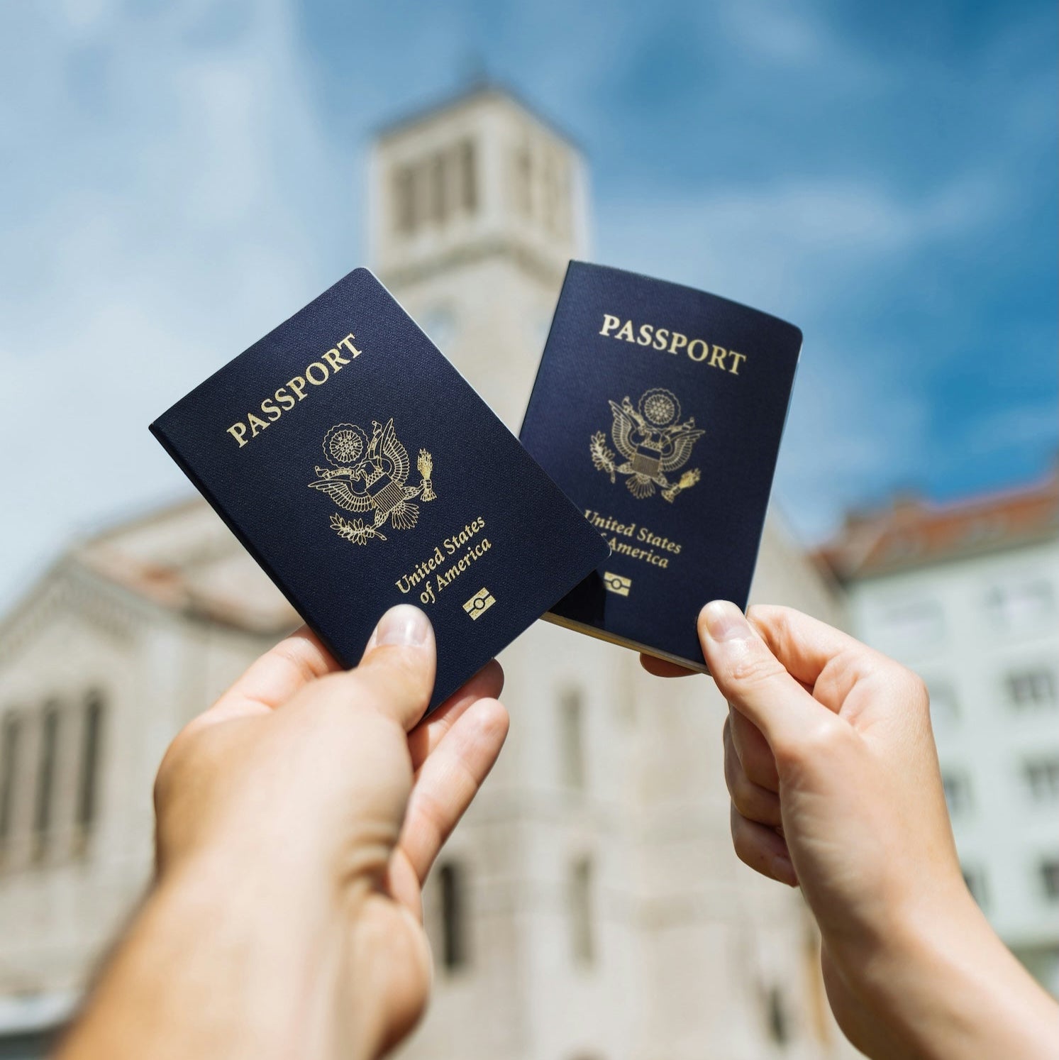 Two passports held up against a blurred architectural background